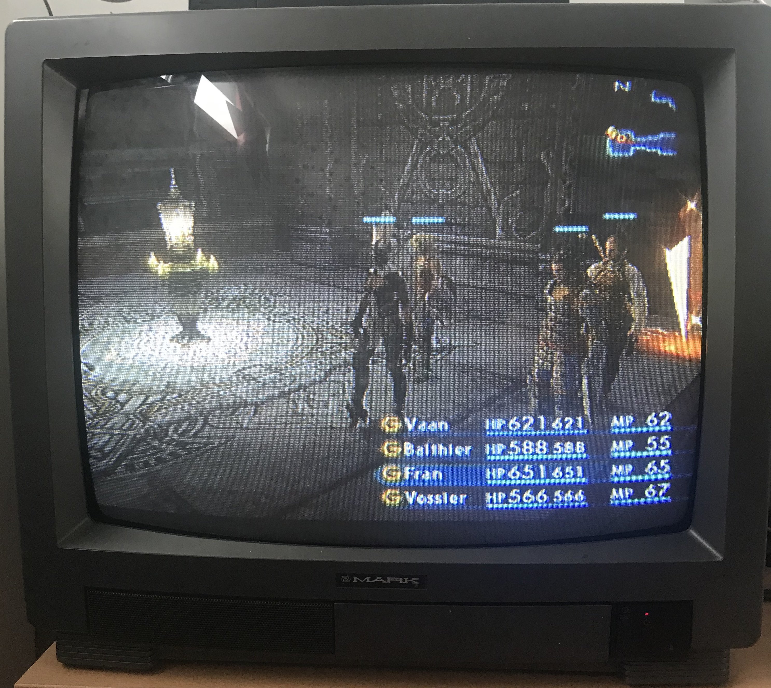 Photo of a square CRT television displaying FINAL FANTASY® XII in standard definition, showing an in-game scene where the characters Vaan (HP 621/621, MP 62), Balthier (HP 588/588, MP 55), Fran (HP 651/651, MP 65) and Vossler (HP 566/566, MP 67) are standing at the entrance of The Tomb of Raithwall.