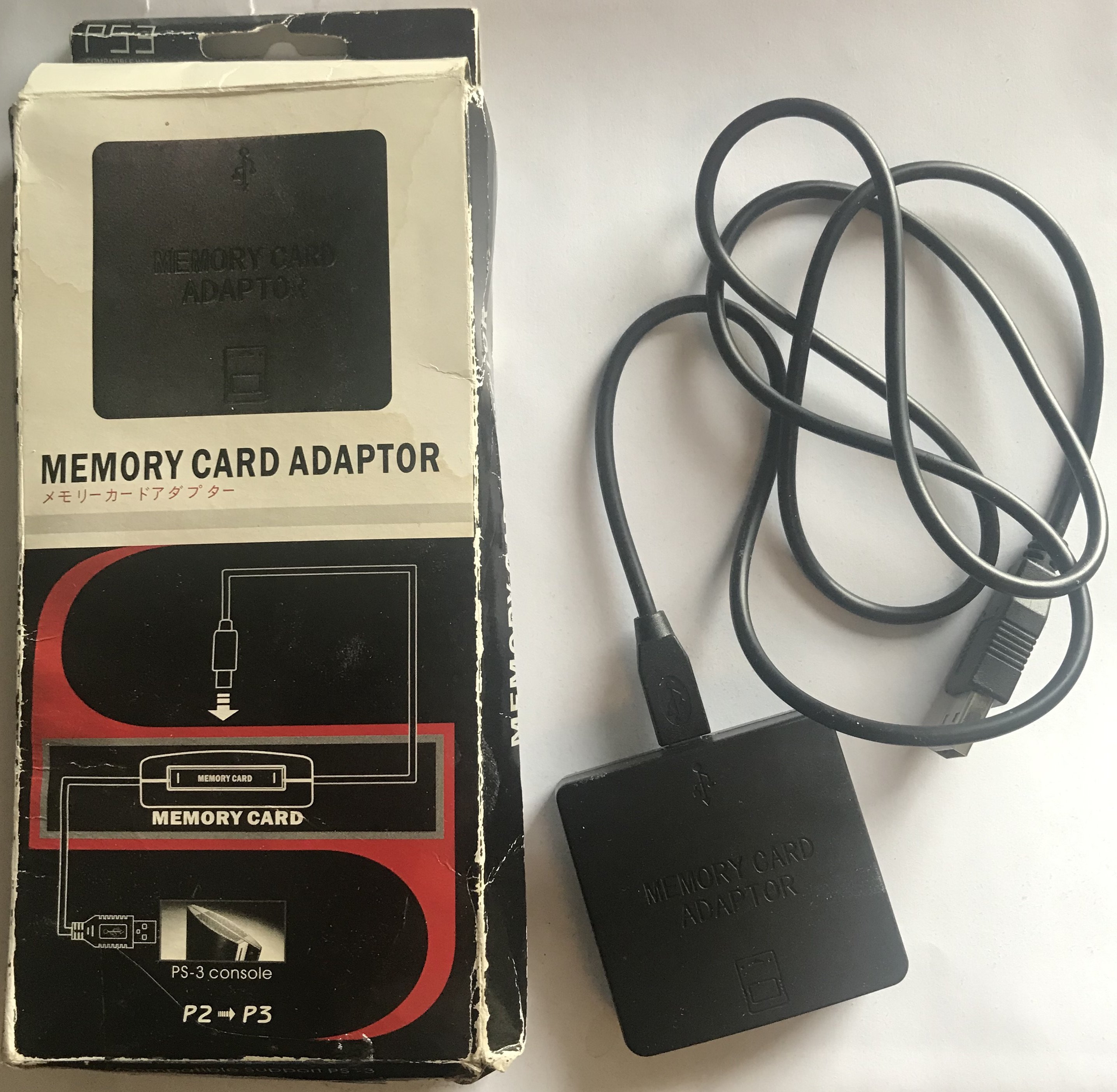 photo of the front of the packaging for a ”Memory Card Adaptor” and the device itself, which is a small black box connected to a USB cable
