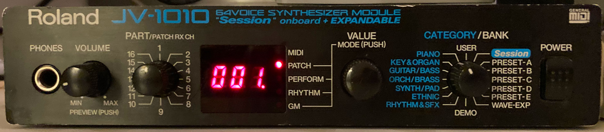 Photo of a “Roland JV-1010 64voice Synthesizer Module” that proudly advertises it has “Session” onboard and is “EXPANDABLE”. This is a half-rack, 1U-high unit similar in size to the SC-88VL, but it has a black metal enclosure rather than plastic. It offers the following set of controls on its front panel, which are quite limited compared to a Sound Canvas or larger JV model: a quarter-inch “Phones” jack; a “Volume” knob; a “Part/Patch” receive channel (abbreviated “RX CH”) rotary switch; a red-on-black three-digit seven-segment LED display (which lists “MIDI”, “Patch”, “Perform”, “Rhythm” and “GM” modes next to it, indicated by an LED that lights up next to it); a “Value” knob (that can also be pushed to select the mode); a “Category/Bank” rotary switch (selecting between “Piano”, “Key&Organ”, “Guitar/Bass”, “Orch/Brass”, “Synth/Pad”, “Ethnic”, “Rhythm&SFX”, “User”, “Demo”, “Wave-Exp” (Wave Expansion), “Session” and five ”Preset” banks); and a “Power” switch.