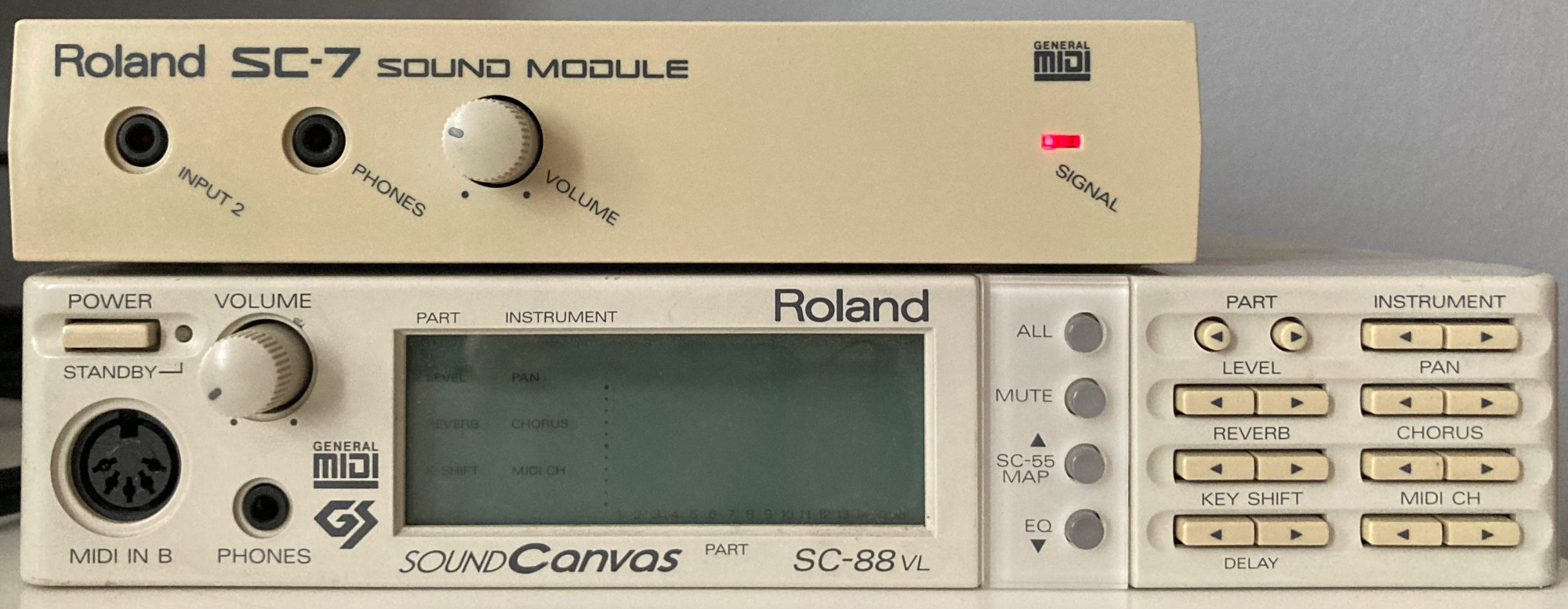 Photo of a Roland SC-7 atop a Roland Sound Canvas SC-88VL. The Roland-SC88VL looks very similar to a Roland SC-55 or SC-55mkII, but this particular model has white plastic rather than dark grey. The Roland SC-7 is smaller than the SC-88VL in all dimensions, being perhaps three quarters the width and height, and it is a gently faded cream colour rather than bright white. The SC-7 lacks the “Sound Canvas” and “GS” branding and has no screen, buttons or additional MIDI port on its front panel, only two 3.5mm jacks (one labelled “Input 2”, one labelled “Phones”), a “Volume” knob, and a small red LED labelled “Signal”. It does, however, have “General MIDI” branding, just like the SC-88VL.
