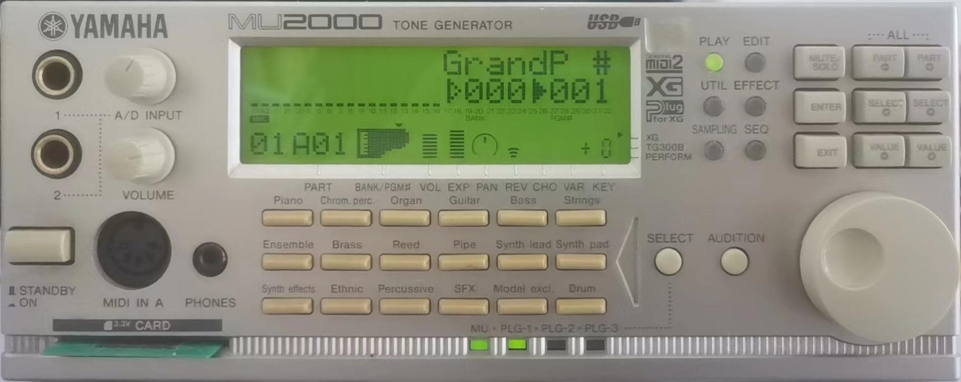 A photo of a “Yamaha MU2000 tone generator”. This is also a half-rack unit, but unlike the MU50 and MU80, it is 2U high, and the overall æsthetic is quite different, because silver is now the colour of everything (no more dark grey plastic). It still has the same bright-green screen and buttons as before at the top, but some of the buttons are now in a chunkier form, and there are now two “A/D Input” quarter-inch jacks rather than one. There is also a huge white encoder wheel, a grid of 6 columns and 3 rows of buttons for selecting different categories of sounds (“Piano”, “Bass”, “Strings” and “SFX” among others), a 3.3-volt SmartMedia card slot and LEDs labelled “MU”, “PLG-1”, “PLG-2” and “PLG-3”. It sports the familiar “XG” logo, but now also has the “General MIDI 2” logo, the “Plug for XG” logo, and a “USB” logo.